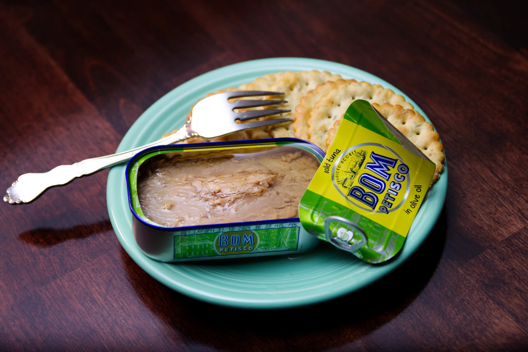 Opened tin of Bom tuna on a plate with crackers