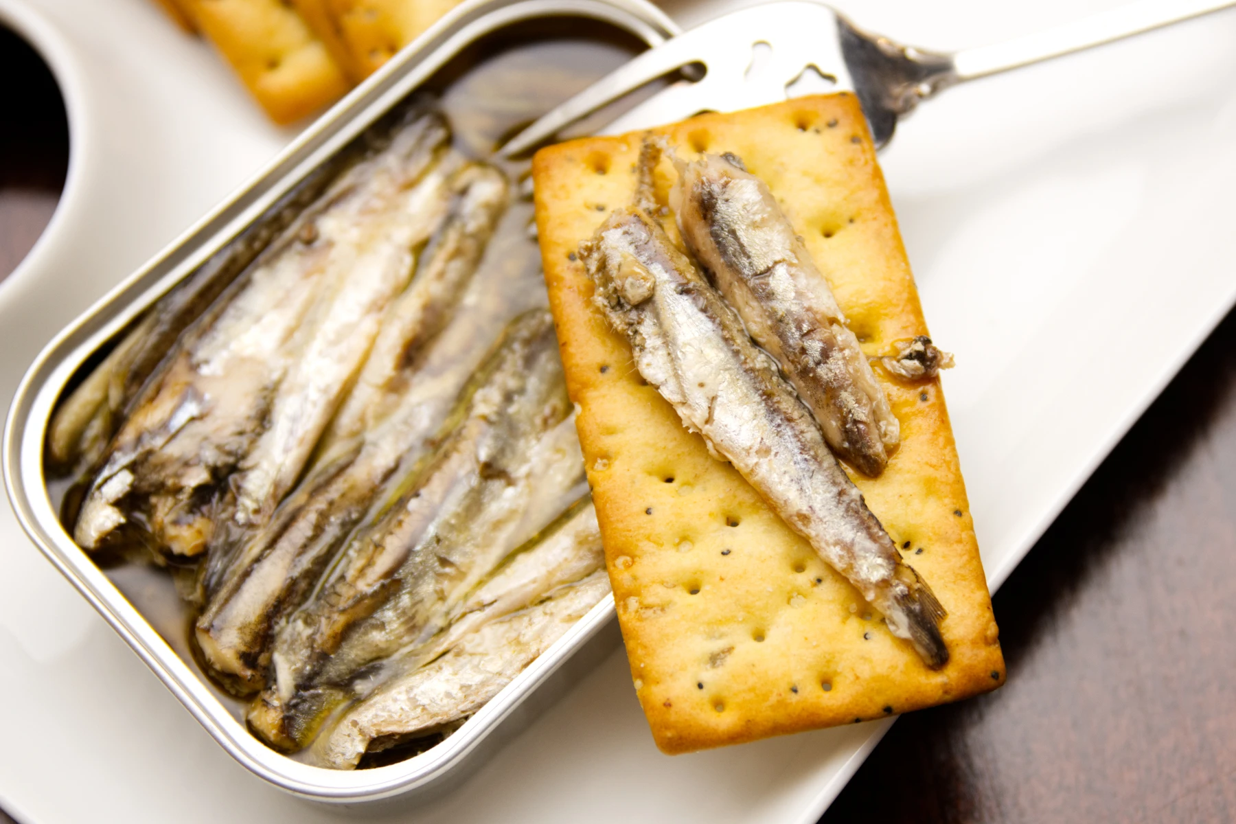 A couple pieces of anchovies on a cracker with the rest of the tin in the background.