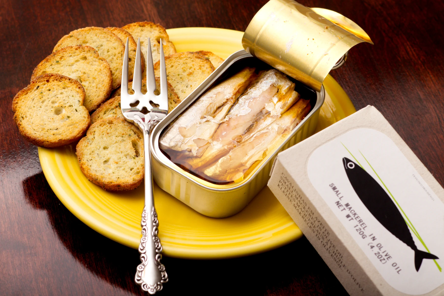 Opened tin of fish with baguette crisps on a plate