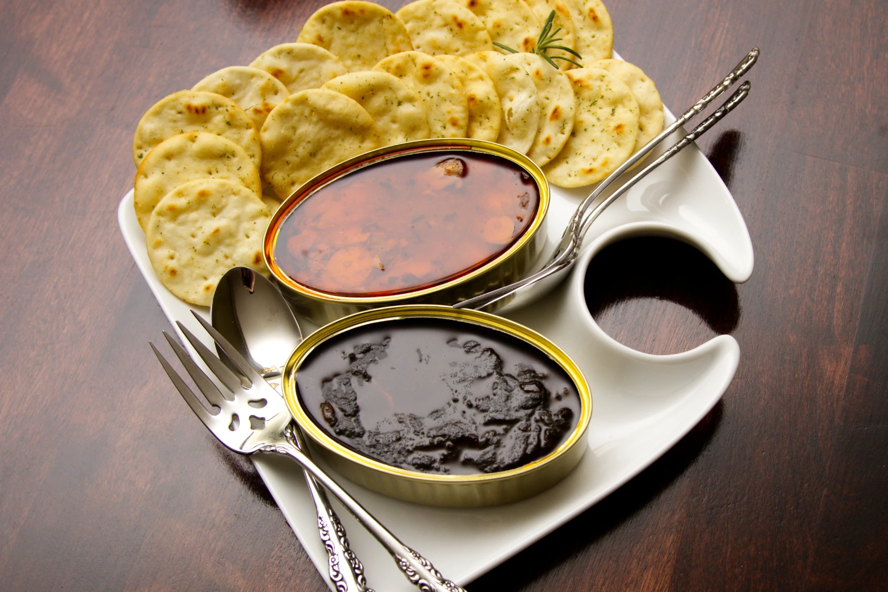 Opened tins of O'Mer brand squid on a plate with crackers.