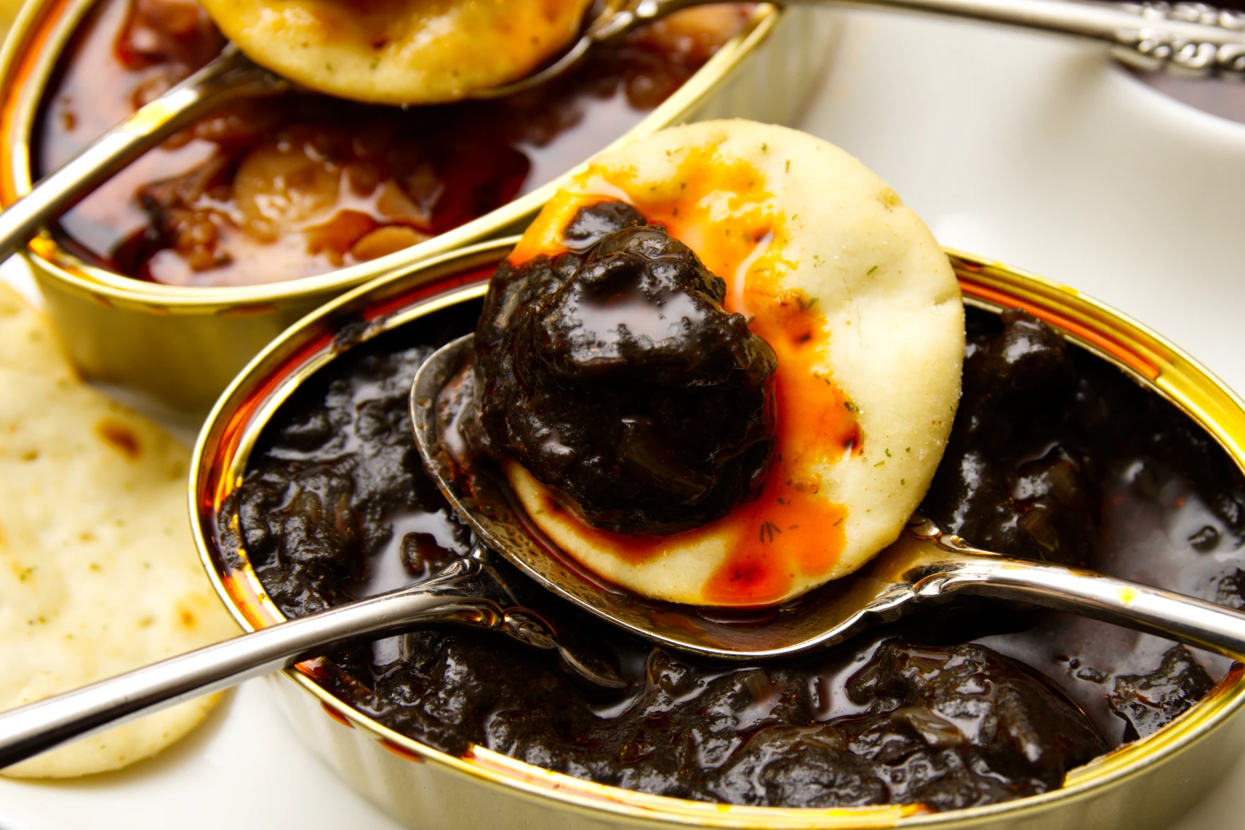 A piece of squid in ink sauce on a cracker.