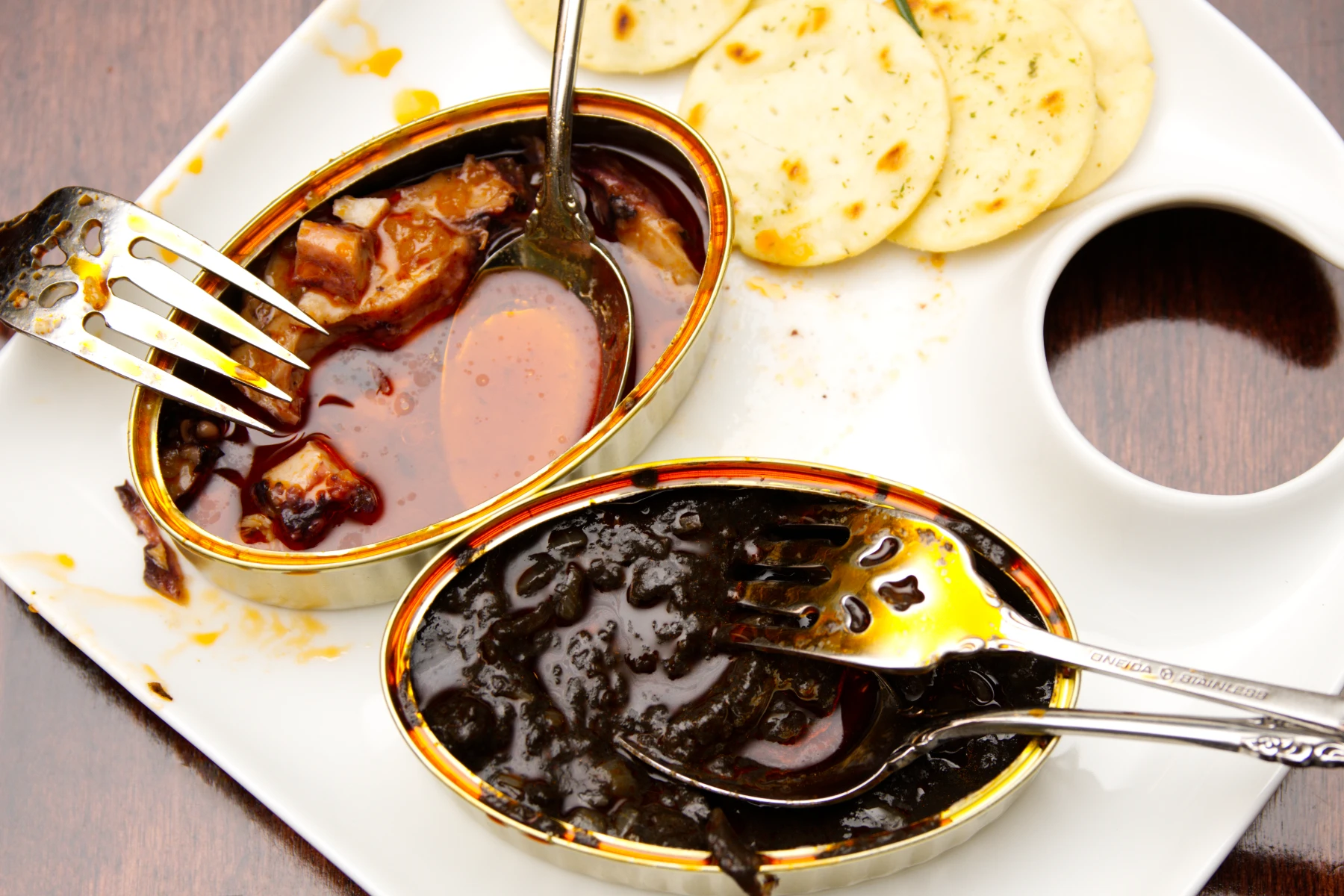 Half-eaten tins of squid on a plate with a few crackers.