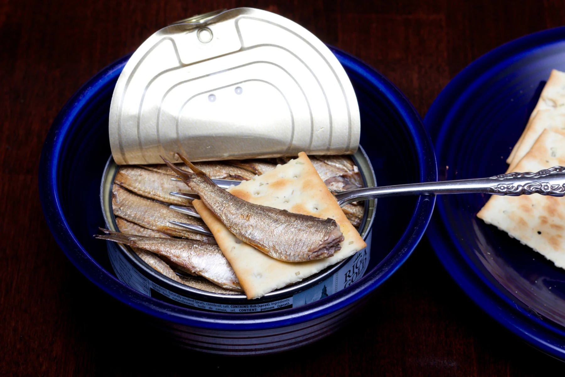 A sprat placed atop a rosemary and seasalt cracker.